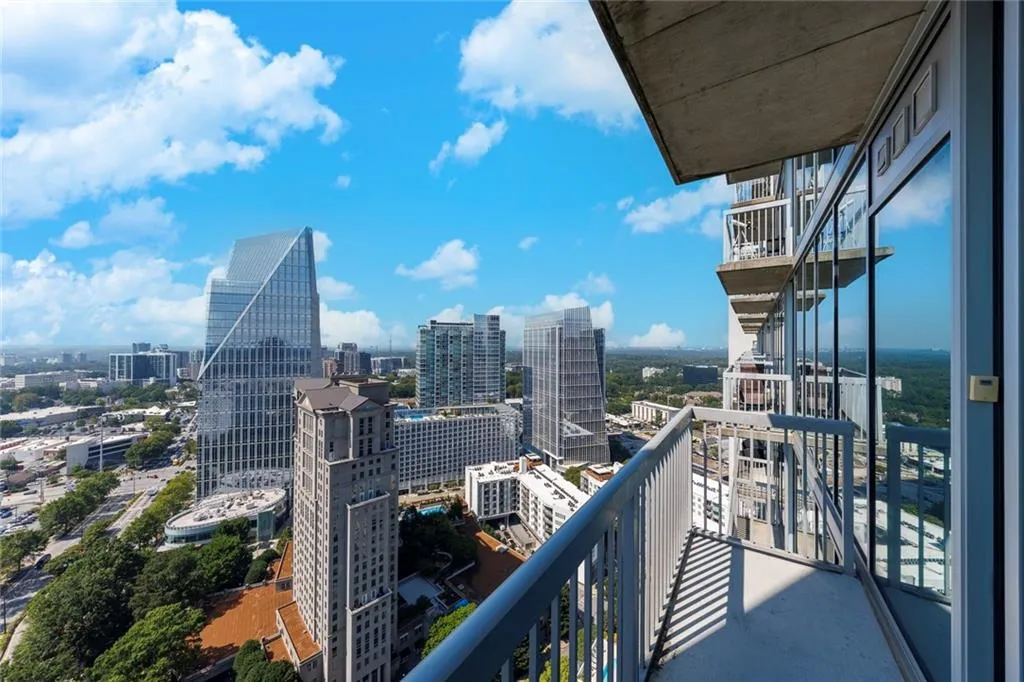 Private balcony with metal railings and concrete flooring, offering expansive city views and a clear sky