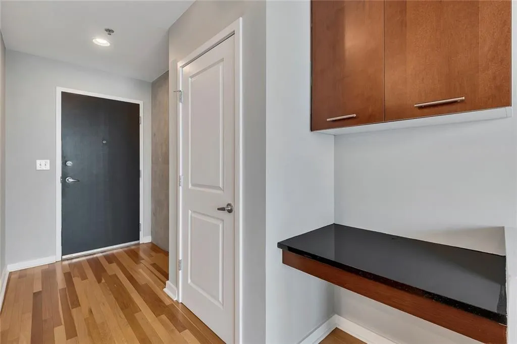 Wood-finish flooring, recessed ceiling lighting, and a built-in desk with a dark countertop, complemented by upper wood-paneled cabinetry