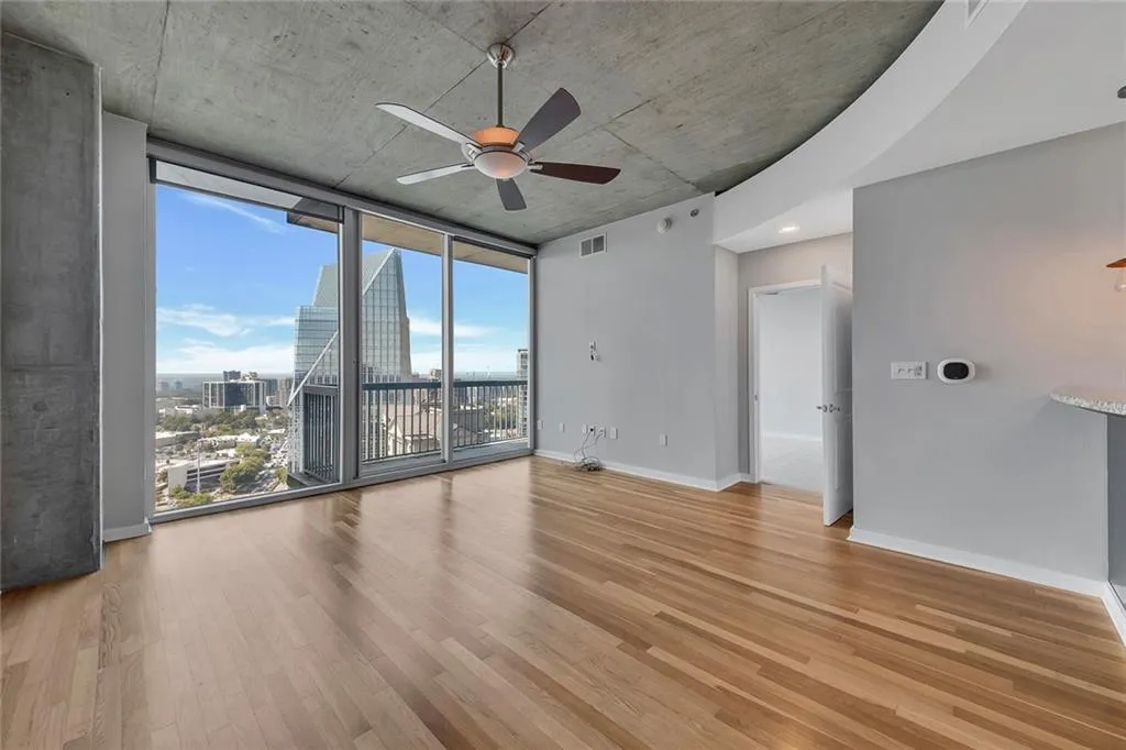 Hardwood-style flooring throughout, concrete ceiling, ceiling fan, and expansive floor-to-ceiling windows with balcony access