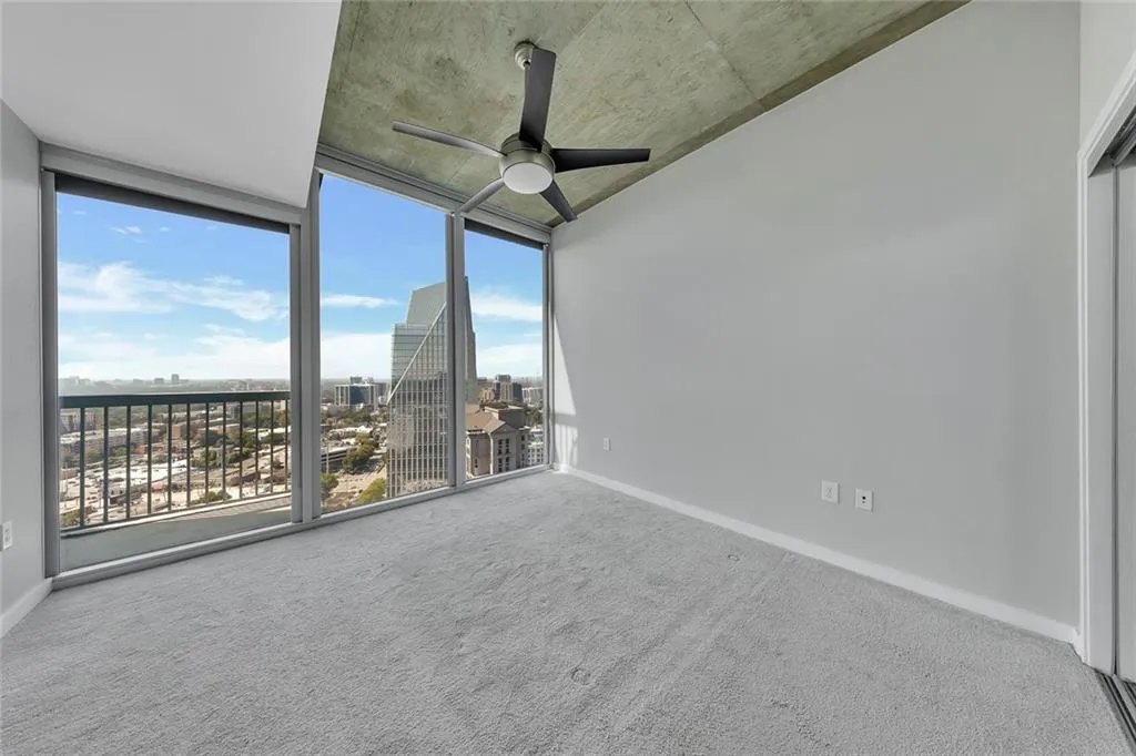 Floor-to-ceiling windows, cityscape scenery, high ceilings, ceiling fan, and light grey carpet