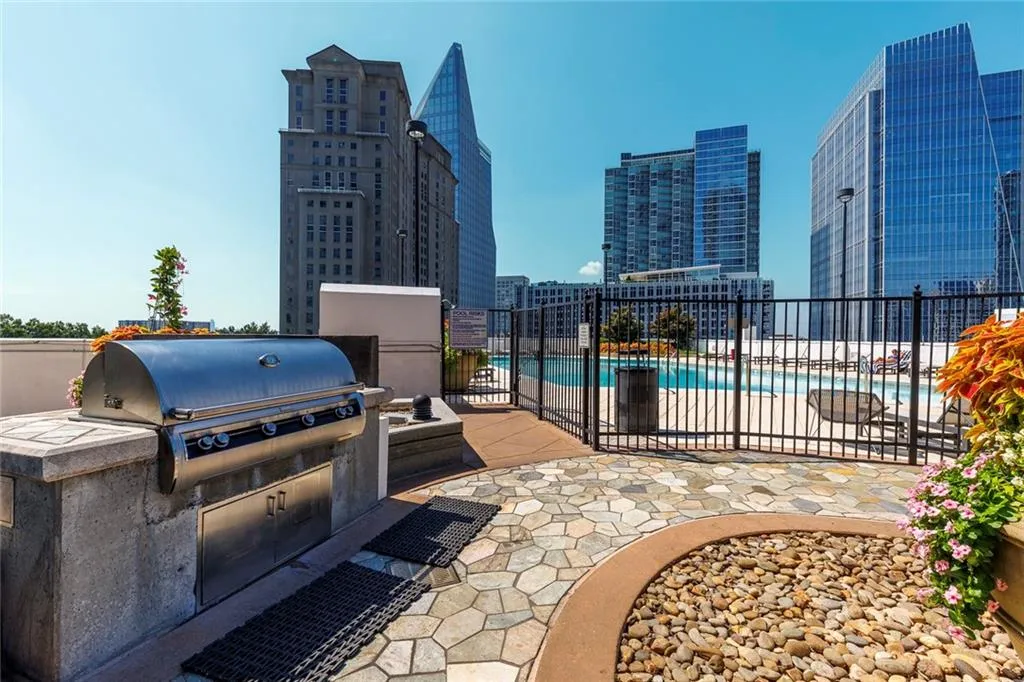 Built-in outdoor grill station, paver stone patio, pebbled landscaping, black metal fencing, and an outdoor swimming pool