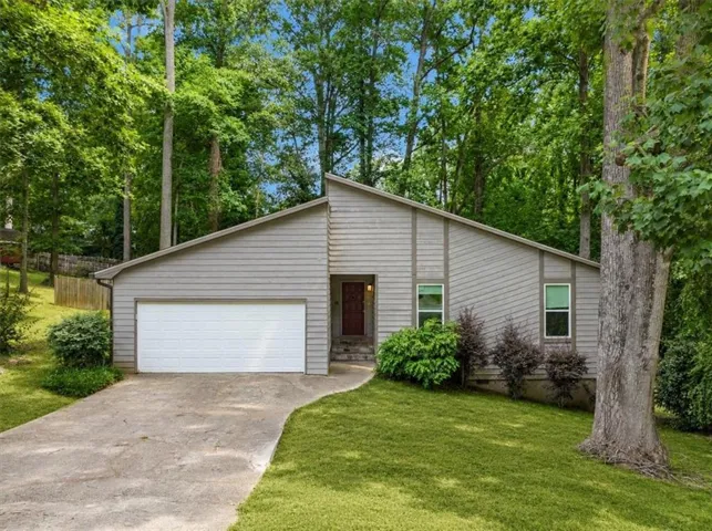 Contemporary-style residence featuring a sloped roofline, attached garage, concrete driveway, mature tree landscaping, and a red entry door