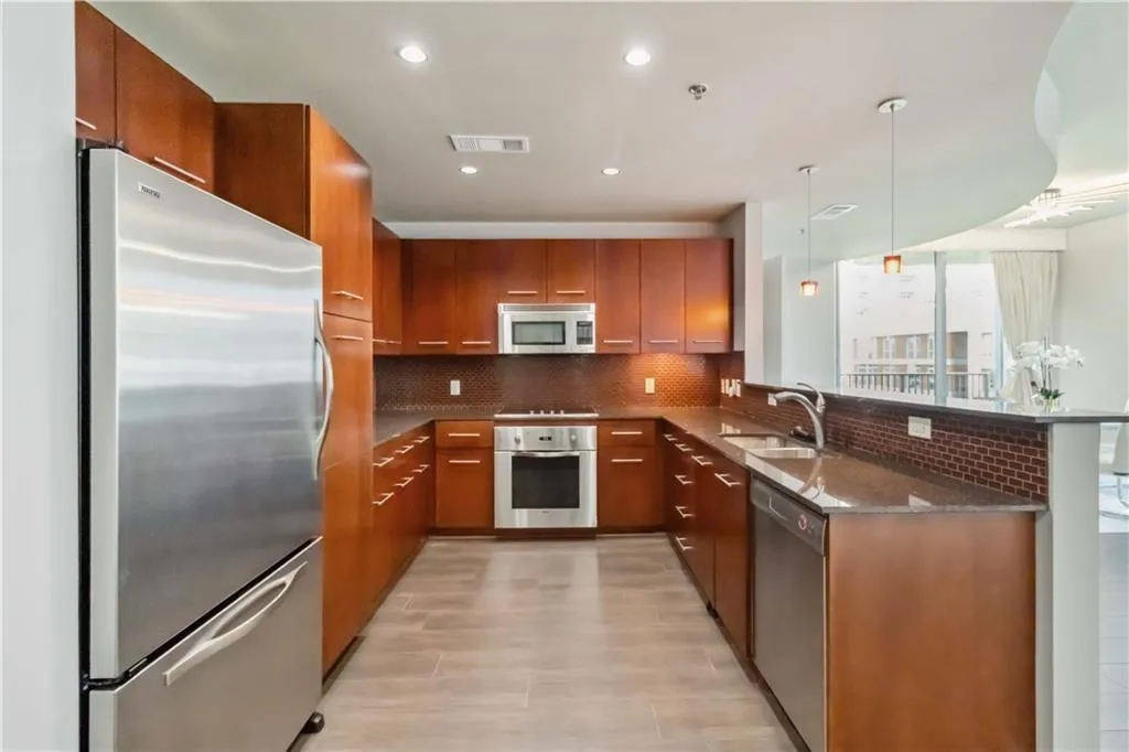 Kitchen with appliances with stainless steel finishes, tasteful backsplash, a peninsula, brown cabinetry, and dark stone counters