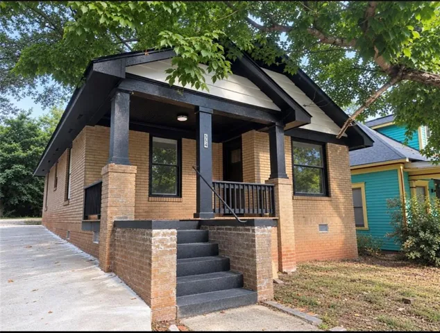 Brick exterior with dark trim and porch railings, concrete driveway, and covered front porch with steps