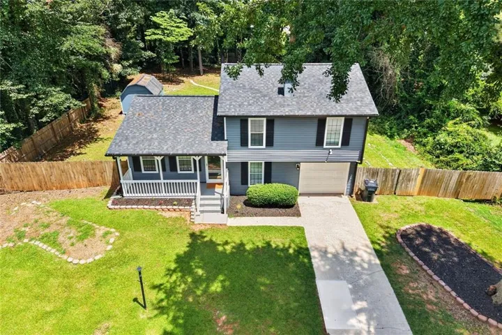 Two-story residence featuring a covered front porch with white railing, a concrete driveway leading to an attached garage, and a fenced perimeter