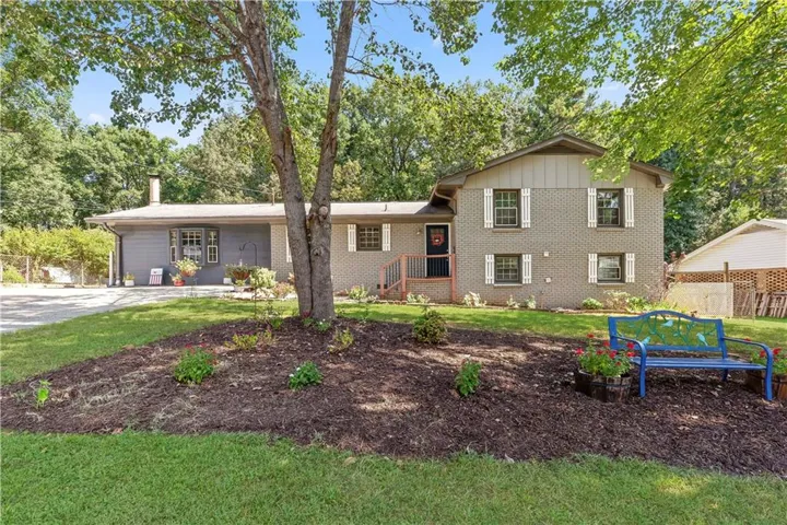 Brick exterior with white shutters, mature trees, landscaped front yard, covered entry, and a gravel driveway