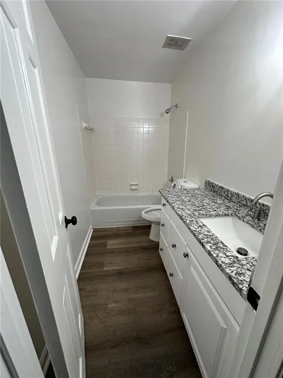 Full bathroom with tiled shower / bath combo, vanity, hardwood / wood-style floors, and toilet
