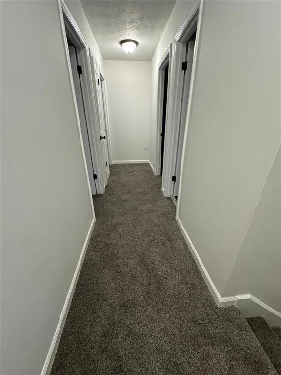 Corridor featuring a textured ceiling and carpet flooring