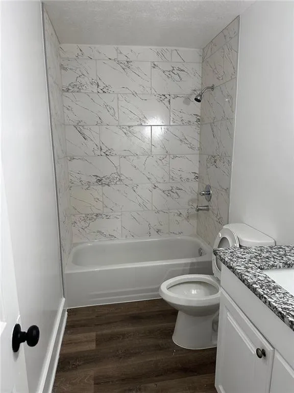 Full bathroom with hardwood / wood-style flooring, tiled shower / bath combo, a textured ceiling, vanity, and toilet