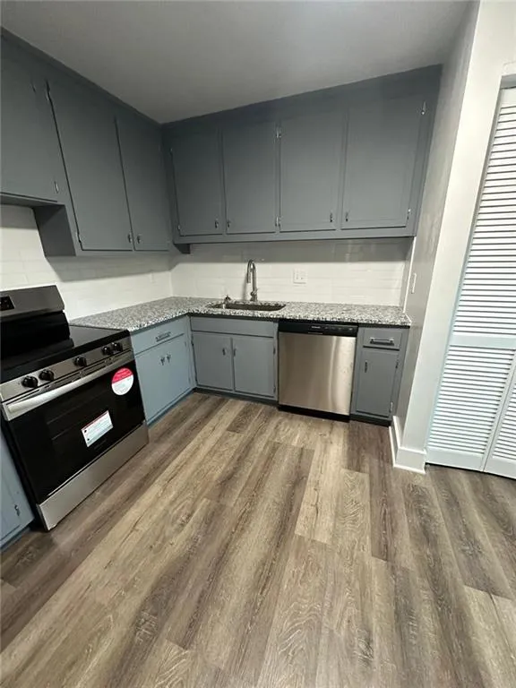 Kitchen featuring dark wood-type flooring, gray cabinetry, appliances with stainless steel finishes, light stone countertops, and sink