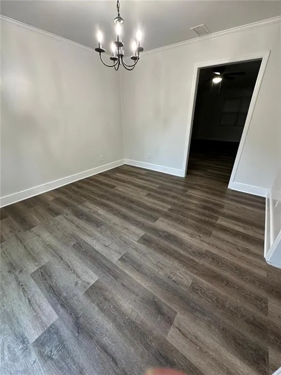 Unfurnished room with a notable chandelier, crown molding, and dark hardwood / wood-style floors