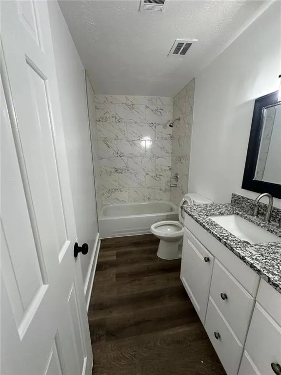 Full bathroom featuring vanity, a textured ceiling, wood-type flooring, toilet, and tiled shower / bath combo