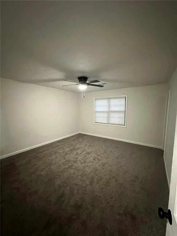Empty room with dark colored carpet and ceiling fan
