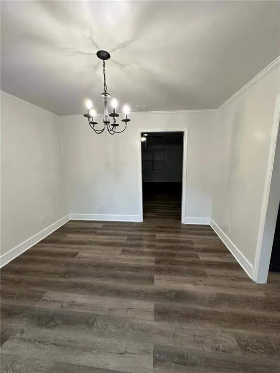 Empty room featuring an inviting chandelier, dark wood-type flooring, and ornamental molding