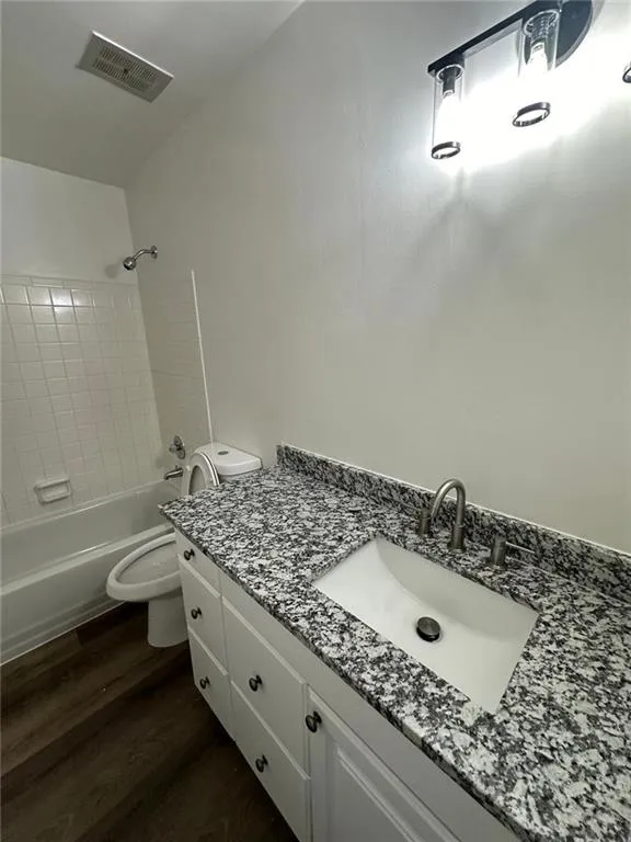 Full bathroom with toilet, tiled shower / bath, wood-type flooring, and vanity