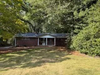 Brick exterior residence featuring a covered front porch, dark-shingle roof, and a grassy front yard
