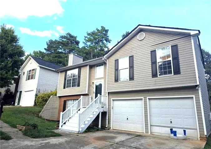 Split-level residence featuring a tan siding exterior and dark shutters