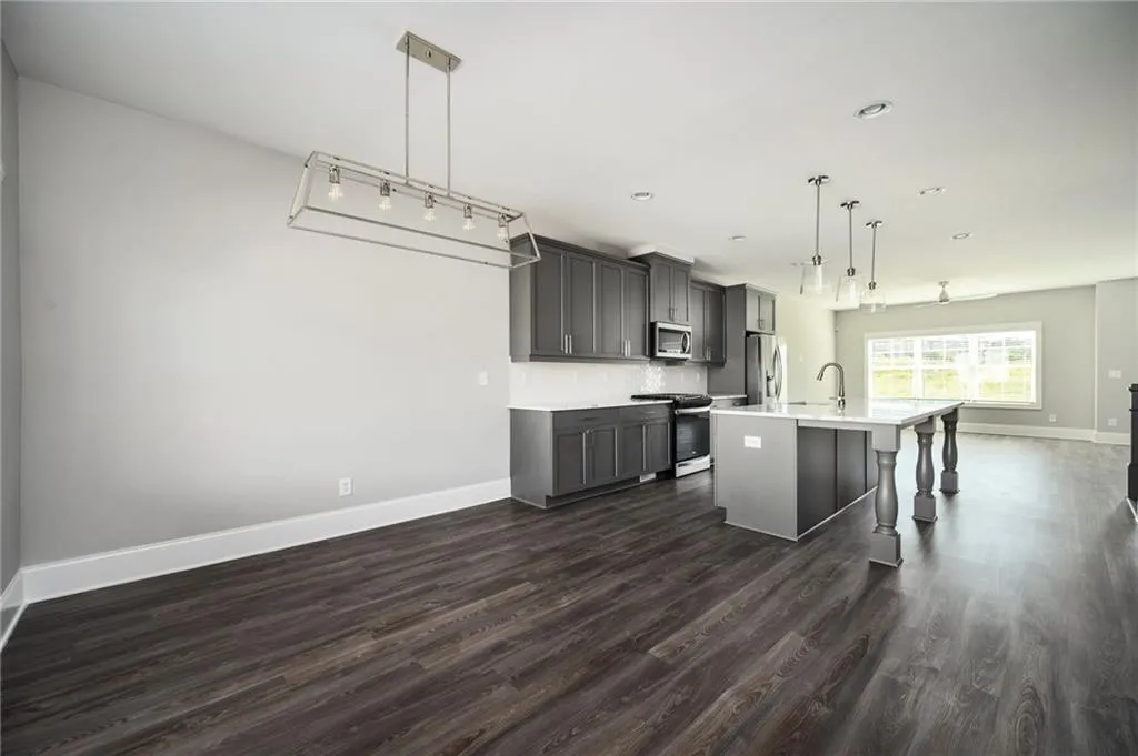Kitchen featuring stainless steel appliances, gray cabinets, light countertops, dark wood-type flooring, and baseboards