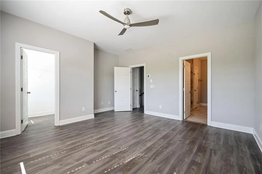 Unfurnished bedroom featuring dark wood-style floors, baseboards, a spacious closet, ensuite bath, and ceiling fan