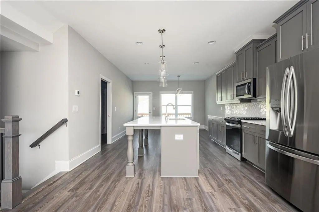 Kitchen featuring stainless steel appliances, a center island with sink, baseboards, dark wood-type flooring, and tasteful backsplash