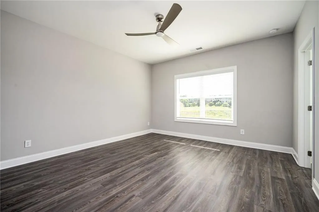 Empty room featuring dark wood-style floors, ceiling fan, baseboards, and a smoke detector