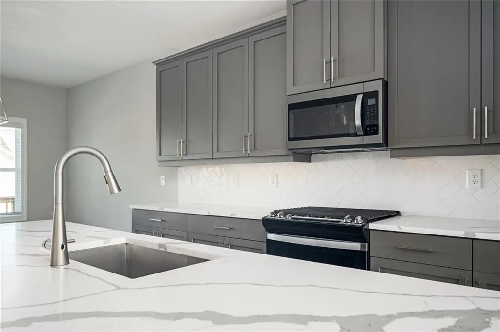 Kitchen with appliances with stainless steel finishes, gray cabinets, a sink, and tasteful backsplash