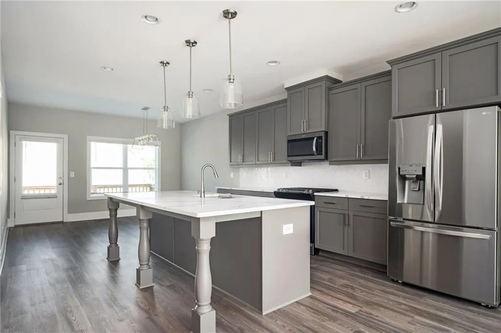 Kitchen with appliances with stainless steel finishes, a sink, gray cabinetry, decorative backsplash, and a center island with sink