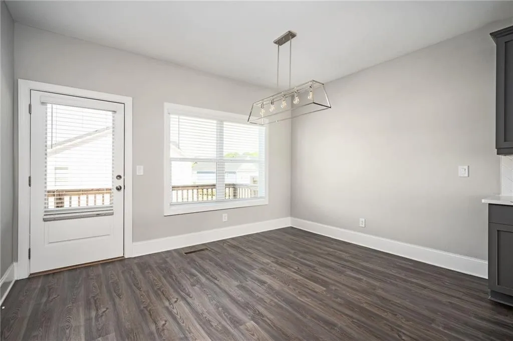 Unfurnished dining area with dark wood-type flooring, baseboards, and a chandelier