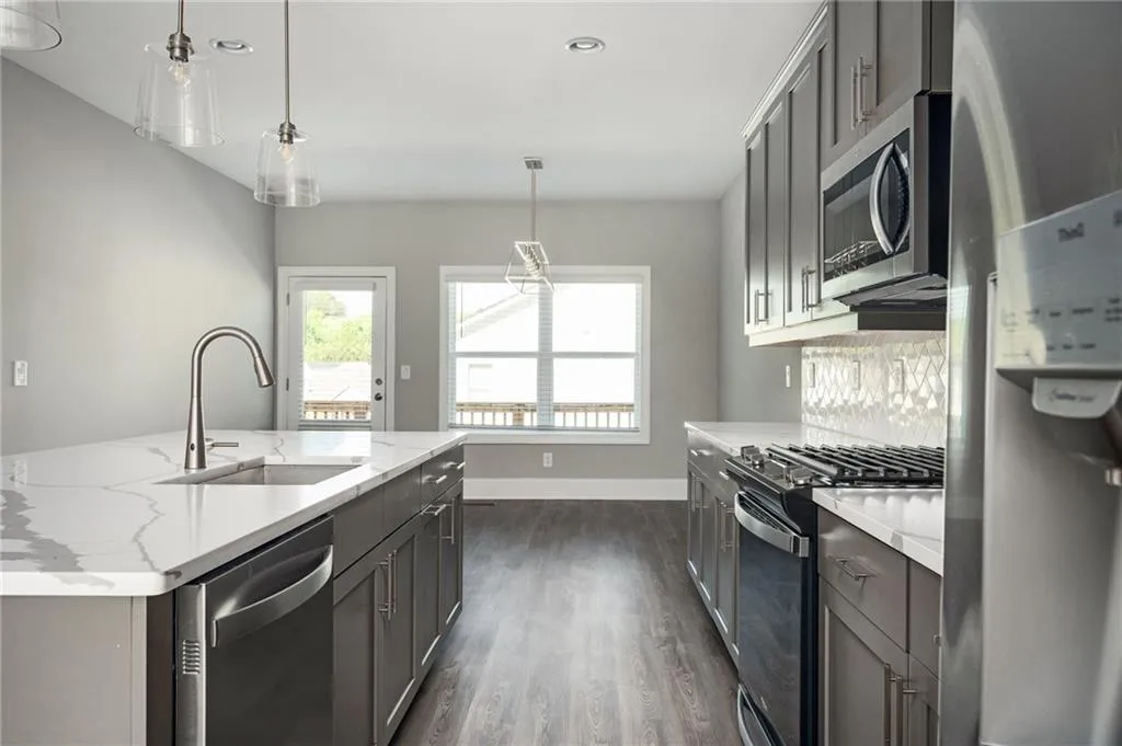 Kitchen featuring appliances with stainless steel finishes, a sink, light stone counters, dark wood-style flooring, and gray cabinets