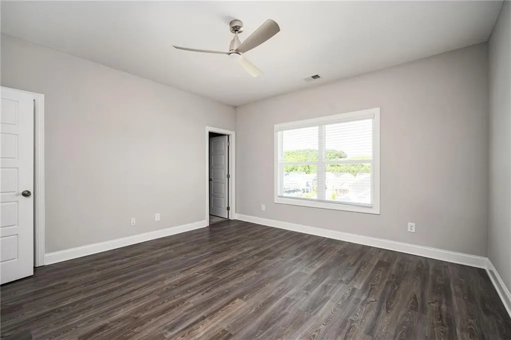 Spare room featuring dark wood-style flooring, a ceiling fan, and baseboards