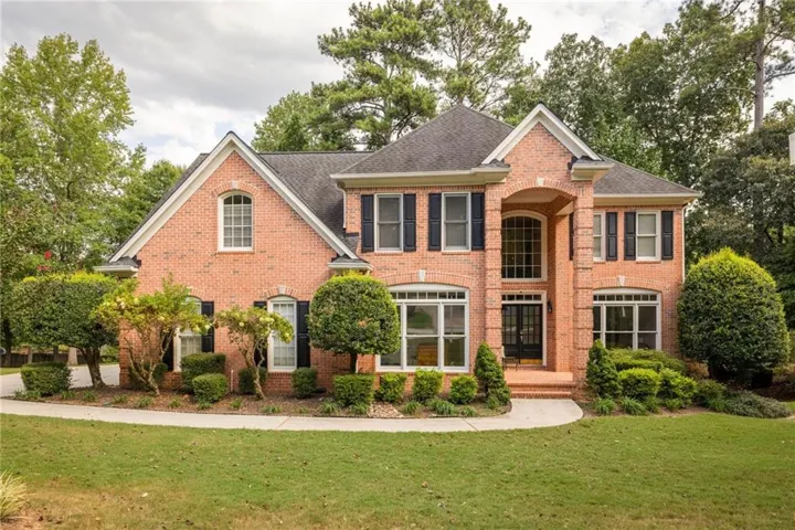 Brick exterior with a prominent arched entry, multiple gables, extensive landscaping, and a paved walkway