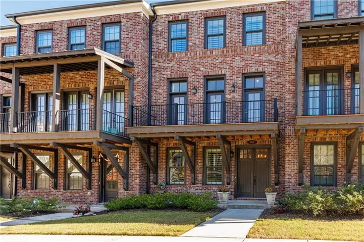 View of front of house with brick siding, a balcony, and a front yard