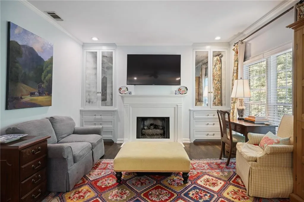 Integrated fireplace with a white mantel, built-in cabinetry with mirrored doors, hardwood flooring, and crown molding