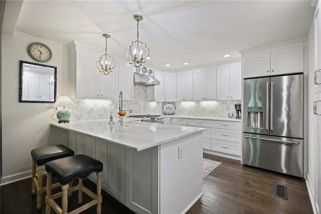Kitchen featuring white cabinetry, a central island with a light-toned countertop, stainless steel appliances, and dark wood-finish flooring