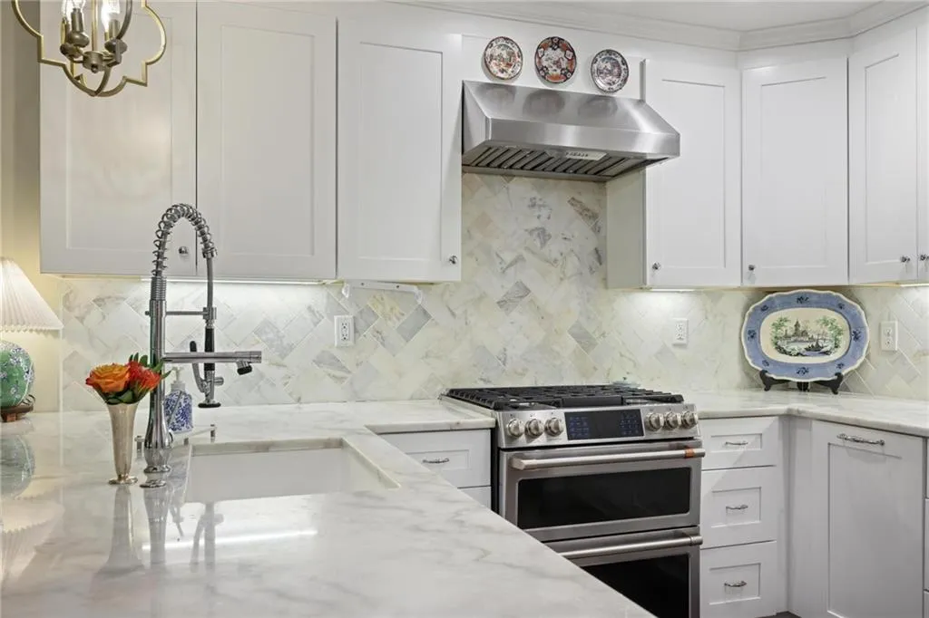 White cabinetry with brushed nickel hardware, stainless steel range with double oven, stainless steel range hood, white countertop, and white tile backsplash