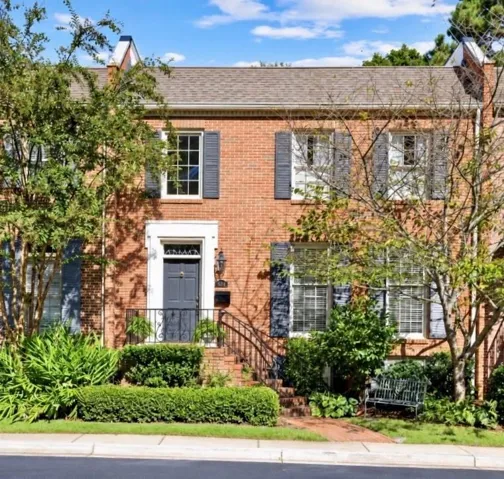 Brick facade with contrasting dark shutters, a prominent entry with a white surround, and mature front landscaping