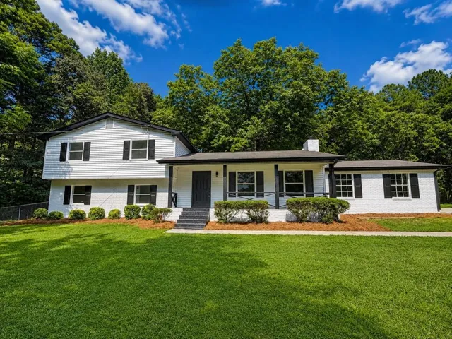 Split-level residence featuring white brick and siding, black shutters, and a covered front porch with dark support columns