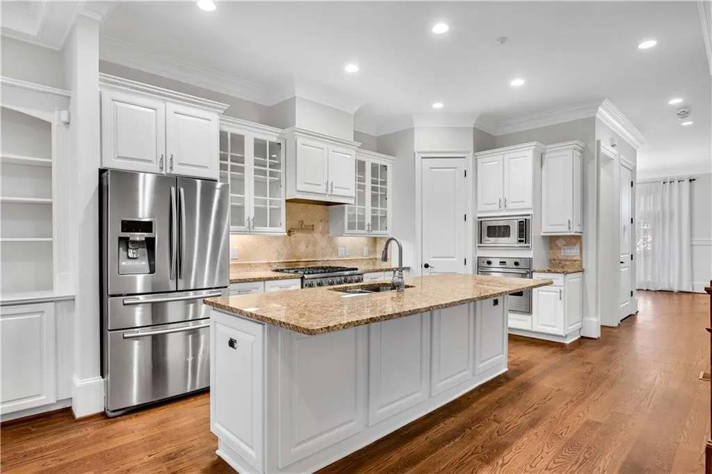 Kitchen with appliances with stainless steel finishes, white cabinetry, and a center island with sink