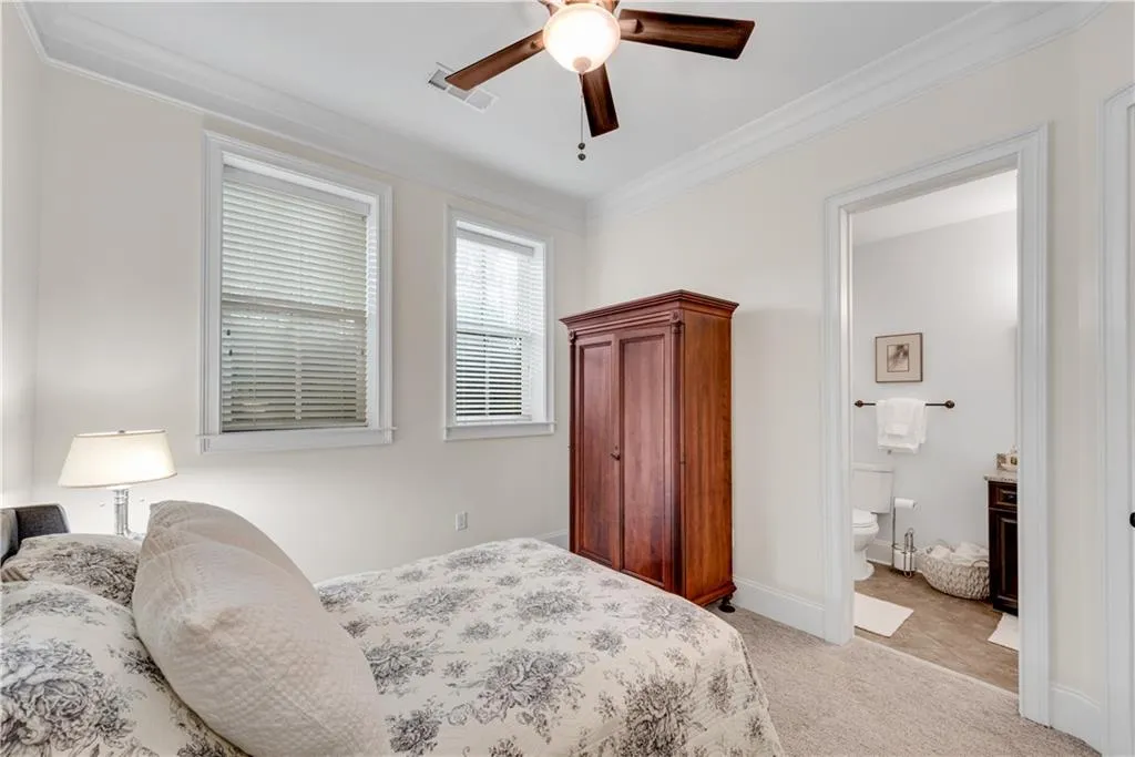 Carpeted bedroom with ornamental molding, ensuite bath, and ceiling fan