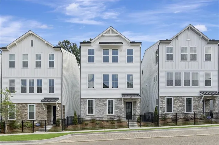 Modern townhome elevation featuring white board and batten siding, stone veneer accents, multiple large windows, a black front door with an awning, and a black metal fence