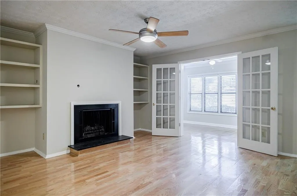 Unfurnished living room featuring built in features, a textured ceiling, a fireplace with raised hearth, crown molding, and light wood-type flooring