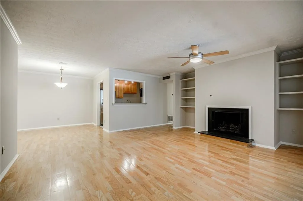 Unfurnished living room featuring crown molding, a textured ceiling, built in shelves, a fireplace with raised hearth, and light wood-style flooring