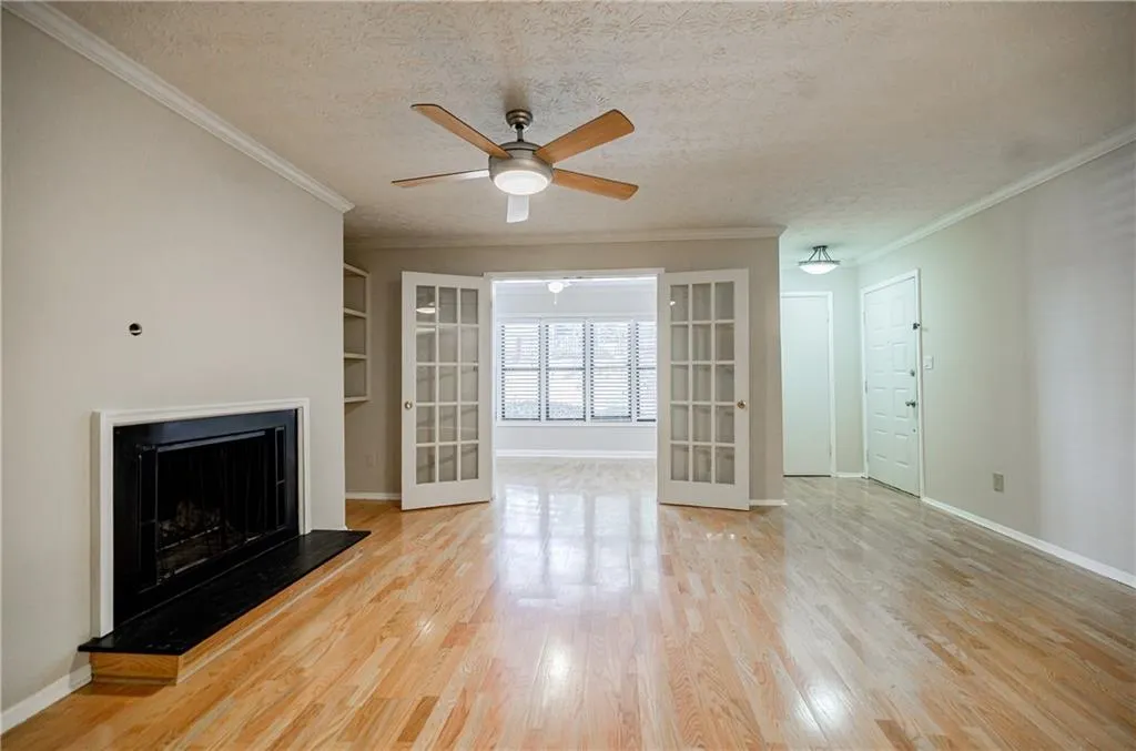 Unfurnished living room featuring a textured ceiling, a fireplace with raised hearth, crown molding, ceiling fan, and light wood-style flooring