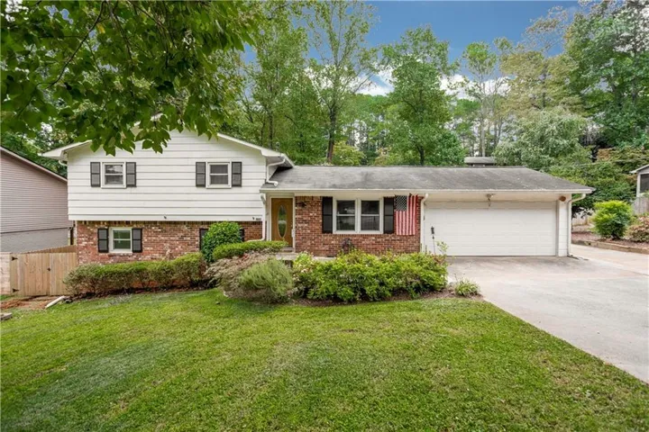 Split-level home featuring a brick and siding exterior, manicured front lawn with mature landscaping, attached two-car garage, and multiple windows providing natural light throughout the facade