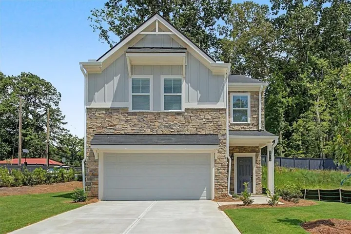 Two-story residence featuring a stone and siding facade, an attached garage, a covered entry, and a paved driveway