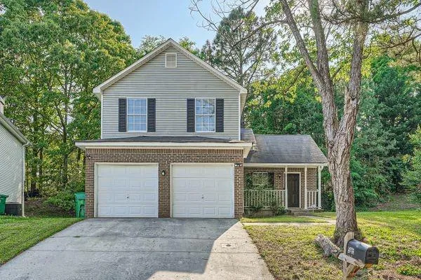 Two-story home featuring a brick facade, dual garage doors, and a covered front porch with white railings