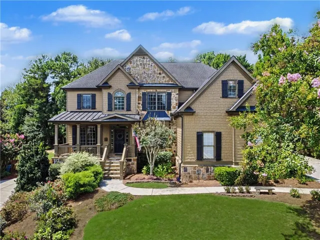 Stone and shingle exterior with dark shutters, covered front porch, and mature landscaping