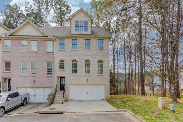 Brick exterior townhome featuring a two-car garage, arched windows on the lower level, and a dormer window on the upper level