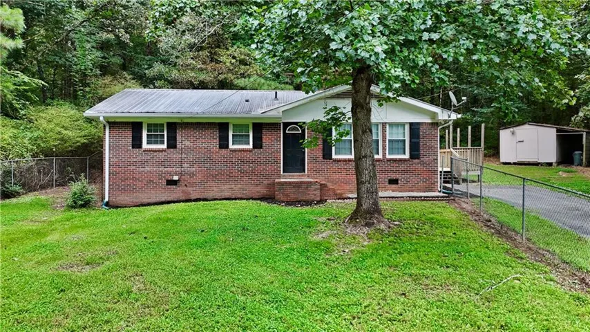Brick-clad exterior with a metal roof, featuring a covered entry, established tree, and a fenced area