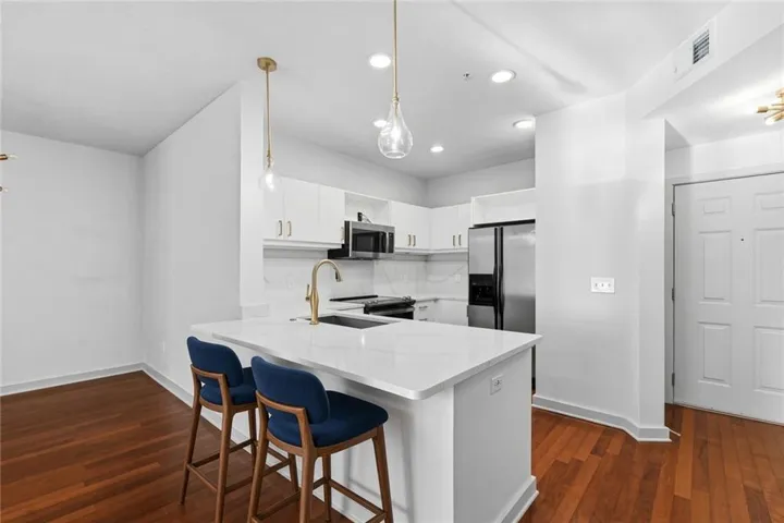 Virtually Staged - White kitchen cabinetry, stainless steel appliances, white countertop island, wood-finish flooring, and recessed ceiling lighting